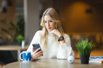 Poradniki - dzielimy się wiedzą | Uniwersytet WSB Merito: Dziewczyna siedząca przy stole z telefonem w dłoni