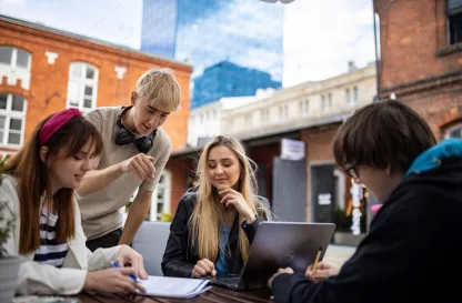 Blog "Okiem Praktyków" | Uniwersytet WSB Merito: Grupa młodych ludzi pracująca przy stole na świeżym powietrzu