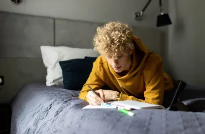 Blog "Okiem Praktyków" | Uniwersytet WSB Merito: Młody chłopak leżący na łóżku spoglądający w notatki