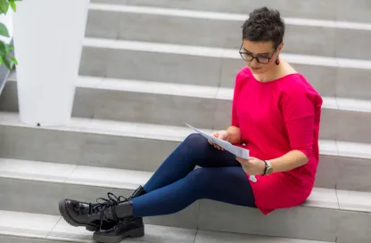 Blog "Okiem Praktyków" | Uniwersytet WSB Merito: Kobieta czytająca książkę siedząc na schodach