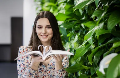 Poradniki - dzielimy się wiedzą | Uniwersytet WSB Merito: Uśmiechnięta dziewczyna z książką, w której robi serce z kartek