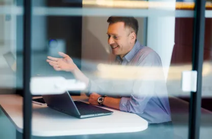 Blog "Okiem Praktyków" | Uniwersytet WSB Merito: Mężczyzna rozmawiający przez kamerkę, zdjęcie robione przez szybę