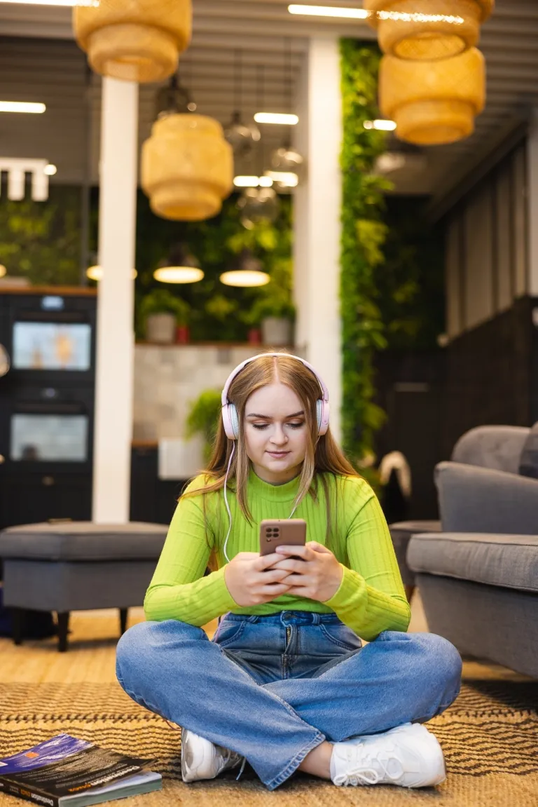 Jakie studia po biol-chemie? Jakie są alternatywy prócz medycyny? | Uniwersytet WSB Merito: Dziewczyna siedząca z telefonem w dłoni, odtwarzająca materiał przez słuchawki