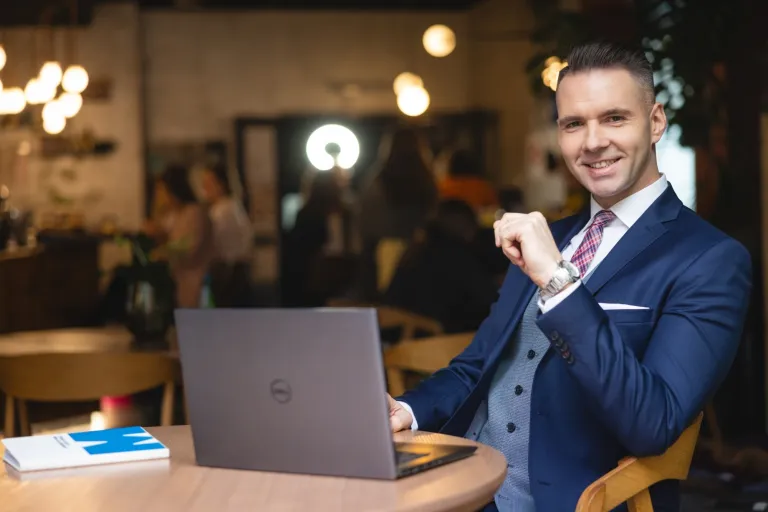 Studia edukacyjne nie tylko dla przyszłych nauczycieli | Uniwersytet WSB Merito: Mężczyzna w garniturze przy stoliku z laptopem