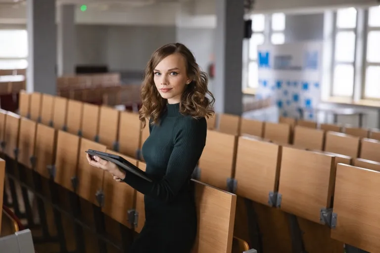 Jaki zawód powinna wybrać osoba introwertyczna? | Uniwersytet WSB Merito: Kobieta stojąca w sali wykładowej, trzyma tablet