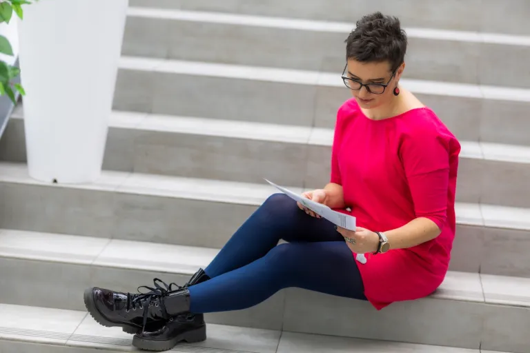 Jak podejmować jakościowe decyzje? | Blog "okiem praktyków" | Uniwersytet WSB Merito: Kobieta czytająca książkę siedząc na schodach