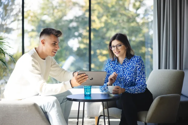 Sztuczna inteligencja w finansach | Blog "okiem praktyków" | Uniwersytet WSB Merito: Dwoje ludzi rozmawiających przy biurku, spoglądających w tableta