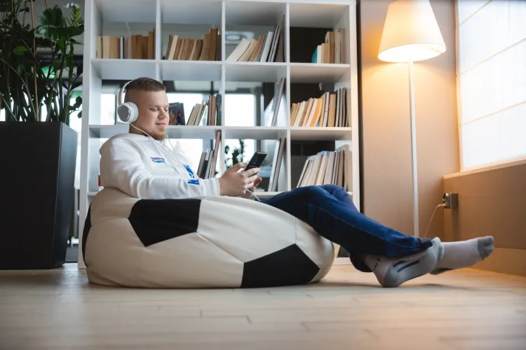 Historia uniwersytetów na świecie. Początki uczelni wyższych | Uniwersytet WSB Merito: Chłopak siedzący na pufie w słuchawkach i z telefonem w dłoni