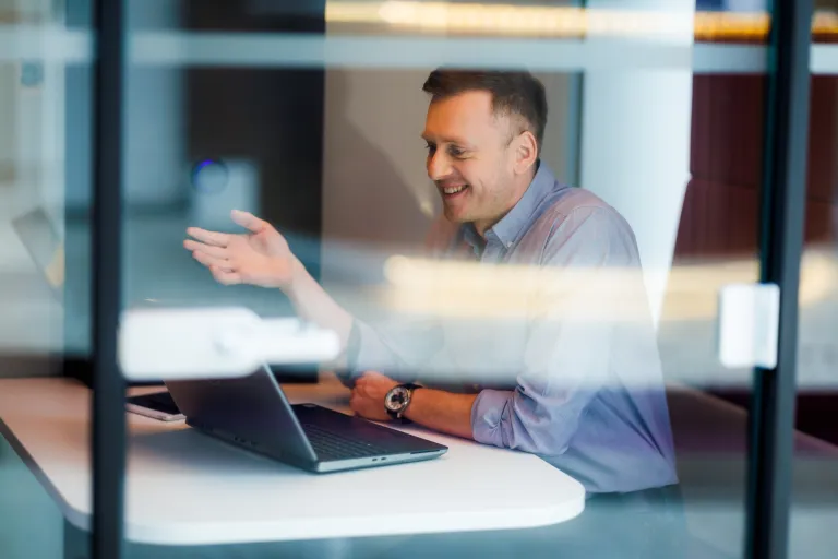 Nagroda Nobla z AI trafia do… | Blog "okiem praktyków" | Uniwersytet WSB Merito: Mężczyzna rozmawiający przez kamerkę, zdjęcie robione przez szybę