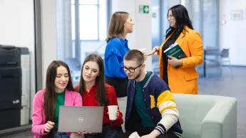 Informatyka | Studia I stopnia w Szczecinie | Uniwersytet WSB Merito Szczecin: Studenci spędzają czas w strefie relaksu, rozmawiając i pracując na laptopie.