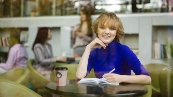 Studentka Uniwersytetu WSB Merito notuje w zeszycie pijąc kawę przy stoliku.