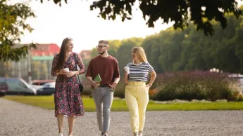 Turystyka i rekreacja | Studia I stopnia w Szczecinie | Uniwersytet WSB Merito Szczecin: Troje studentów Uniwersytetu WSB Merito Szczecin spaceruje po parku, trzymając kawę i rozmawiając.