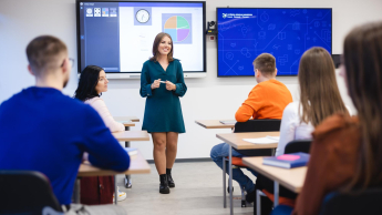 Przygotowanie pedagogiczne – dla nauczycieli przedmiotów lub zajęć prowadzonych w szkole podstawowej i ponadpodstawowej | Studia podyplomowe w Szczecinie | Uniwersytet WSB Merito Szczecin: Studentka Uniwersytetu WSB Merito prowadzi prezentację w sali wykładowej, a pozostali studenci słuchają jej wystąpienia.