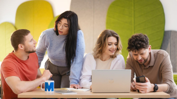 grupa studentów w kolorowej sali pracuje przy laptopie