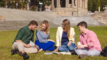 Pedagogika | Studia II stopnia w Szczecinie | Uniwersytet WSB Merito Szczecin: Grupa studentów siedzi na trawie i wspólnie uczy się z książek w plenerze.