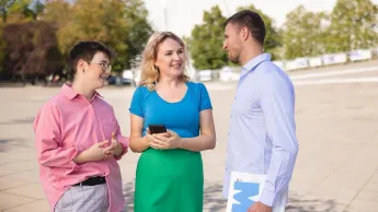 Pedagogika opiekuńczo-wychowawcza i resocjalizacja | Studia I stopnia w Szczecinie | Uniwersytet WSB Merito Szczecin: Trzy osoby rozmawiają na placu przed nowoczesnym budynkiem.
