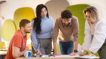 Grupa studentów pracuje nad projektem przy stole, analizując notatki i szkice.
