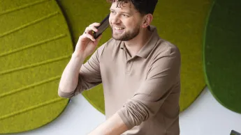 Menedżer logistyki | Studia II stopnia w Szczecinie | Uniwersytet WSB Merito Szczecin: Student rozmawia przez telefon w nowoczesnej przestrzeni uczelni, z laptopem i notatkami na biurku.
