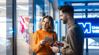 Dwoje studentów omawia projekt przy tablicy z kolorowymi notatkami, w tle widoczne logo Uniwersytetu WSB Merito.