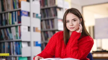 Trychologia | Studia podyplomowe w Szczecinie | Uniwersytet WSB Merito Szczecin: Studentka siedzi w bibliotece, czytając książkę.