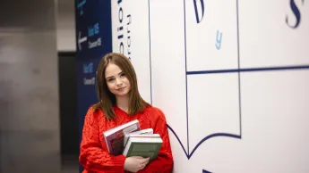 Finanse publiczne i podatki | Studia II stopnia ze studiami podyplomowymi  | Uniwersytet WSB Merito Szczecin: Studentka z książkami przy bibliotece, gotowa do nauki