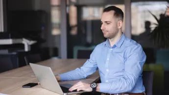 Wyniki wyszukiwania | Uniwersytet WSB Merito Szczecin: Mężczyzna pracuje przy laptopie w nowoczesnej sali konferencyjnej, skupiony na ekranie.