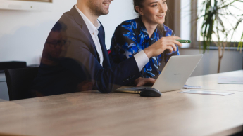 Zarządzanie przedsiębiorstwem | Studia I stopnia w Szczecinie | Uniwersytet WSB Merito Szczecin: Dwie osoby siedzą przy stole w sali konferencyjnej, pracując wspólnie przy laptopie.