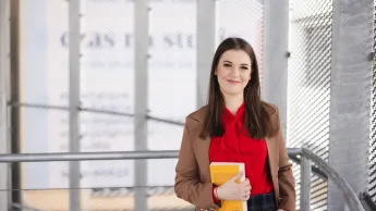 Administracja publiczna | Studia podyplomowe w Szczecinie | Uniwersytet WSB Merito Szczecin: Uśmiechnięta studentka w budynku uczelni trzyma książkę