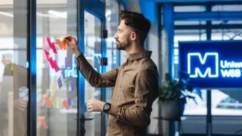Inteligentne technologie sprzedaży i marketingu | Studia I stopnia w Szczecinie | Uniwersytet WSB Merito Szczecin: Osoba na tle logo Uniwersytet Merito