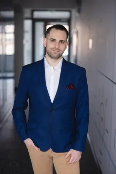 Maturzyści | Uniwersytet WSB Merito Szczecin: Student Uniwersytetu WSB Merito stoi na korytarzu, elegancko ubrany.