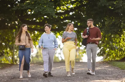 Aktualności | Uniwersytet WSB Merito Szczecin: Czworo studentów spaceruje alejką w parku, rozmawiając i uśmiechając się.