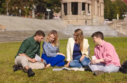 Aktualności | Uniwersytet WSB Merito Szczecin: Grupa studentów siedzi na trawie i wspólnie uczy się z książek w plenerze.