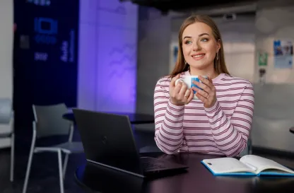 Aktualności | Uniwersytet WSB Merito Szczecin: Dziewczyna z kubkiem siedzi przy laptopie przy stoliku.