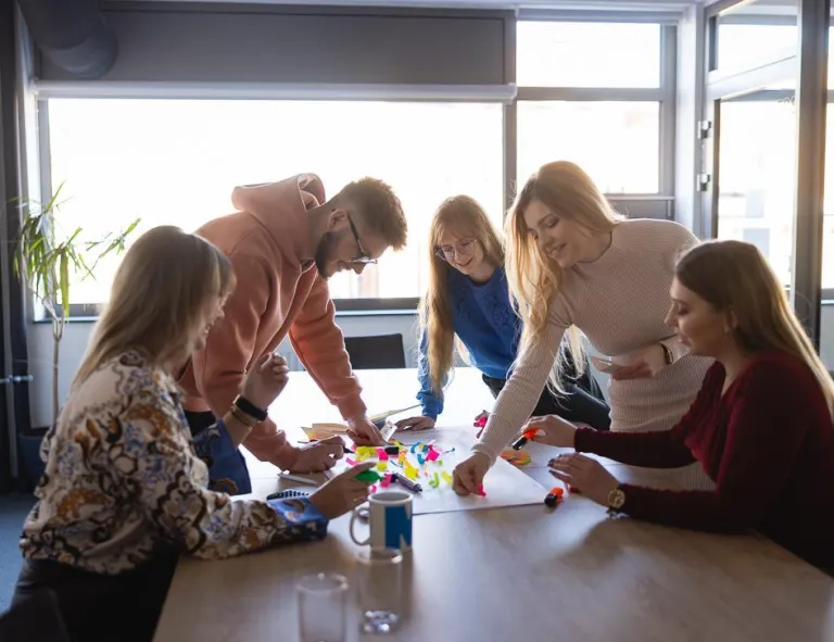 Wpływ społeczny | Uniwersytet WSB Merito Szczecin: Grupa studentów wspólnie pracuje nad kreatywnym projektem, używając kolorowych karteczek i markerów.