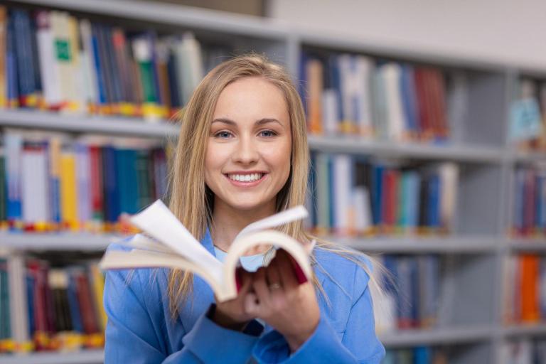 Wydawnictwa naukowe KK | Uniwersytet WSB Merito Szczecin: Studentka Uniwersytetu WSB Merito wertuje książkę w bibliotece.