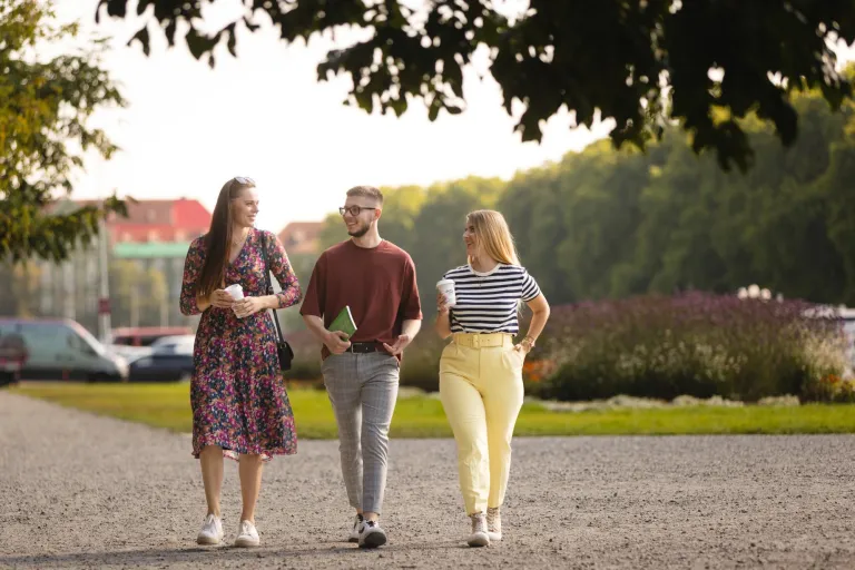 Controlling w biznesie | Studia podyplomowe w Szczecinie | Uniwersytet WSB Merito Szczecin: Troje studentów Uniwersytetu WSB Merito Szczecin spaceruje po parku, trzymając kawę i rozmawiając.