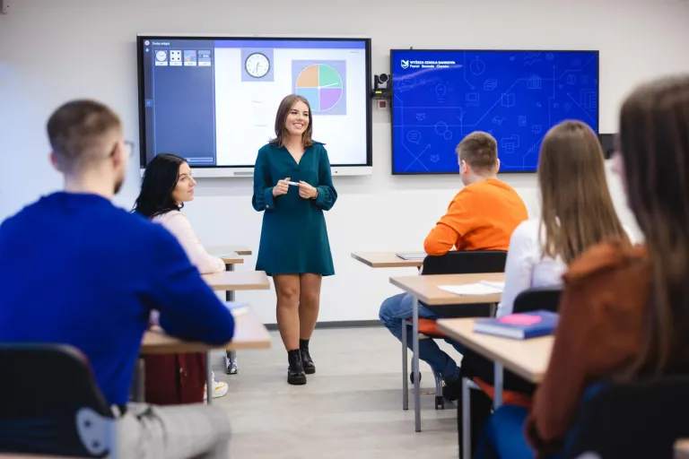Szkoły | Uniwersytet WSB Merito Szczecin: Studentka Uniwersytetu WSB Merito prowadzi prezentację w sali wykładowej, a pozostali studenci słuchają jej wystąpienia.