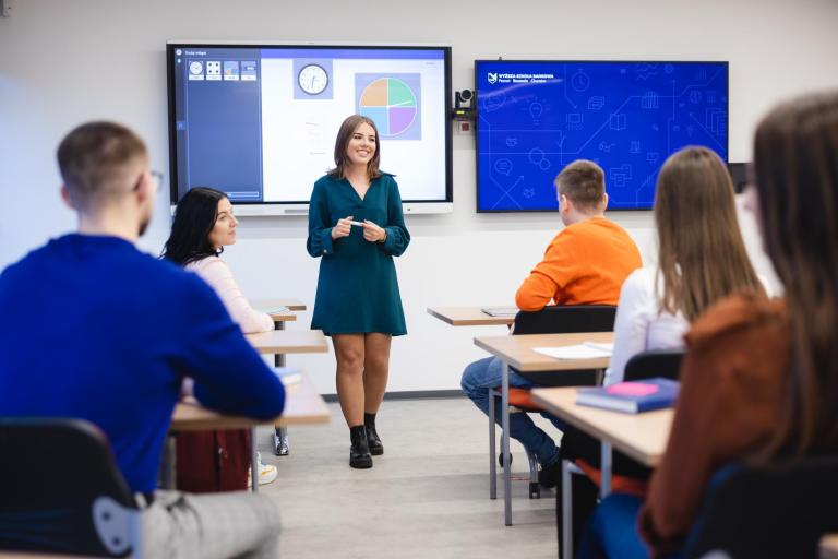 Szkoły | Uniwersytet WSB Merito Szczecin: Studentka Uniwersytetu WSB Merito prowadzi prezentację w sali wykładowej, a pozostali studenci słuchają jej wystąpienia.