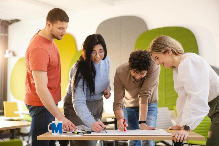 Szkoły | Uniwersytet WSB Merito Szczecin: Cztery osoby wspólnie pracują nad projektem, zapisując pomysły na kartce.