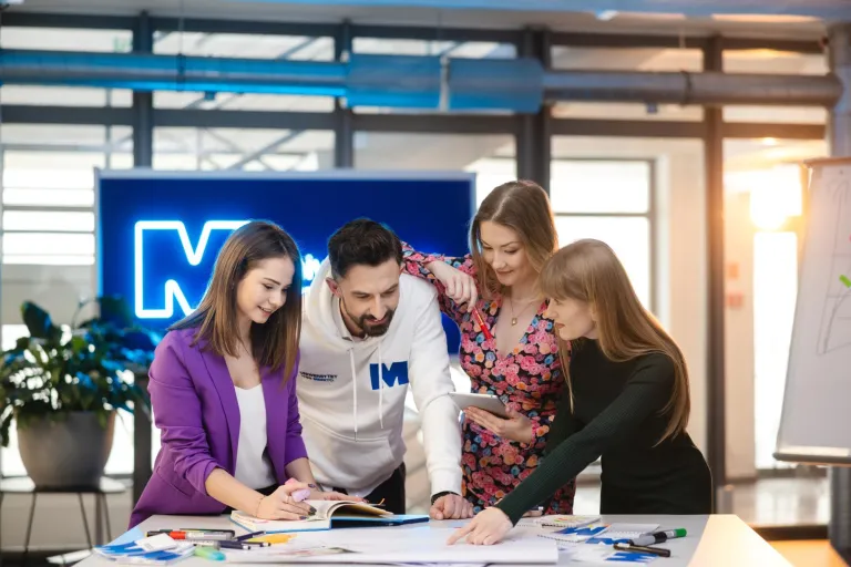 Budowa i utrzymanie aplikacji no-code | Studia podyplomowe w Szczecinie | Uniwersytet WSB Merito Szczecin: Czworo studentów Uniwersytetu WSB Merito wspólnie pracuje nad projektem przy tablecie.