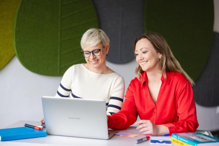 Pośrednictwo pracy | Uniwersytet WSB Merito Szczecin: Dwie kobiety pracują przy laptopie, uśmiechając się i omawiając materiały.