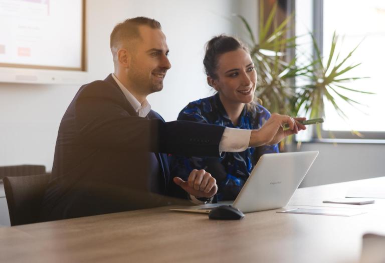 Dział Studiów Podyplomowych i Szkoleń | Uniwersytet WSB Merito Szczecin: Dwie osoby pracują przy laptopie, omawiając prezentację.