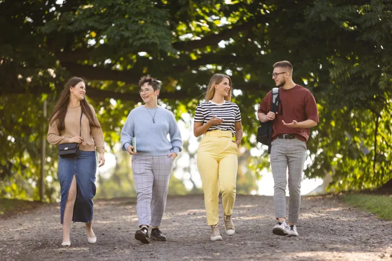 Czesne, stypendia i zniżki | Uniwersytet WSB Merito Szczecin: Czworo studentów spaceruje alejką w parku, rozmawiając i uśmiechając się.