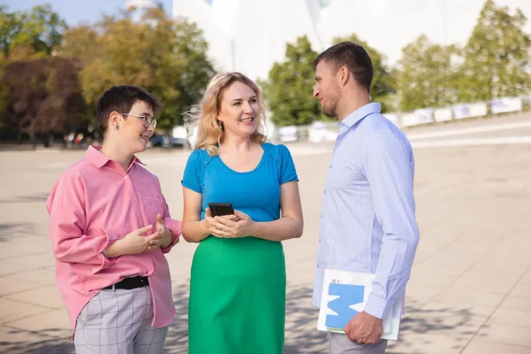 Terapia pedagogiczna | Studia II stopnia w Szczecinie | Uniwersytet WSB Merito Szczecin: Trzy osoby rozmawiają na placu przed nowoczesnym budynkiem.