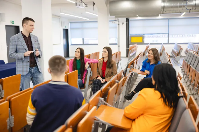 Dietetyka i promocja zdrowia | Studia I stopnia w Szczecinie | Uniwersytet WSB Merito Szczecin: Wykładowca rozmawia ze studentami w auli, prowadząc swobodne zajęcia w małej grupie.