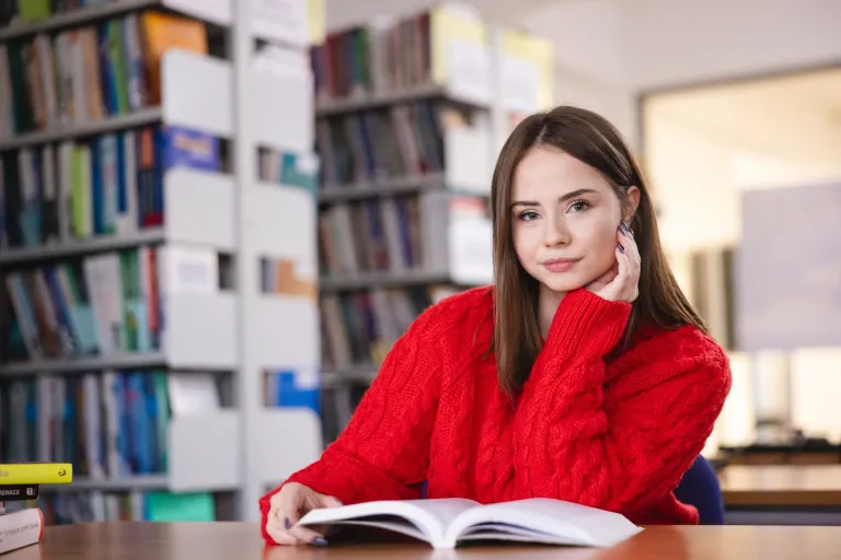 Dydaktyka języków obcych | Studia podyplomowe w Szczecinie | Uniwersytet WSB Merito Szczecin: Studentka siedzi w bibliotece, czytając książkę.
