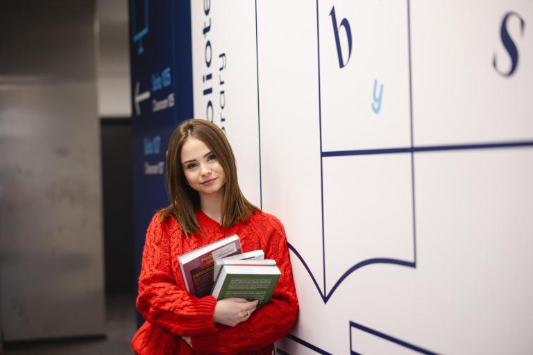 Kosmetologia | Studia I stopnia w Szczecinie | Uniwersytet WSB Merito Szczecin: Studentka z książkami przy bibliotece, gotowa do nauki