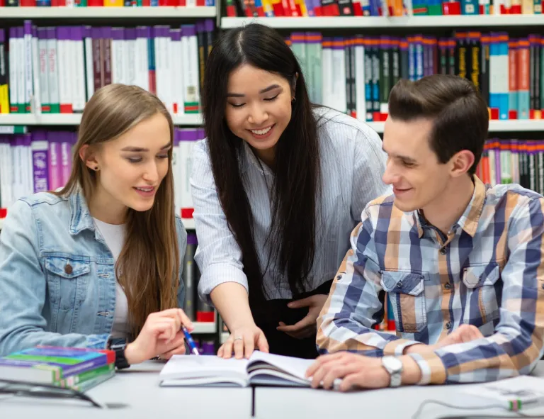 Pedagogika opiekuńczo-wychowawcza i terapia zajęciowa | Studia I stopnia w Szczecinie | Uniwersytet WSB Merito Szczecin: Studenci uczą się razem przy stole w bibliotece.