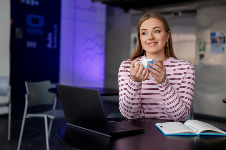 Program Very Important Student | Uniwersytet WSB Merito Szczecin: Dziewczyna z kubkiem siedzi przy laptopie przy stoliku.