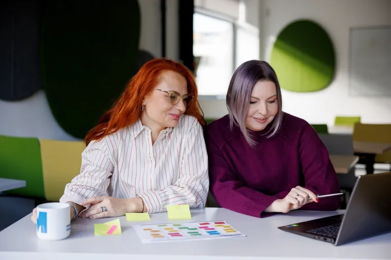 Wczesne wspomaganie rozwoju | Studia podyplomowe w Szczecinie | Uniwersytet WSB Merito Szczecin: Dwie kobiety pracują przy laptopie i kolorowych notatkach.